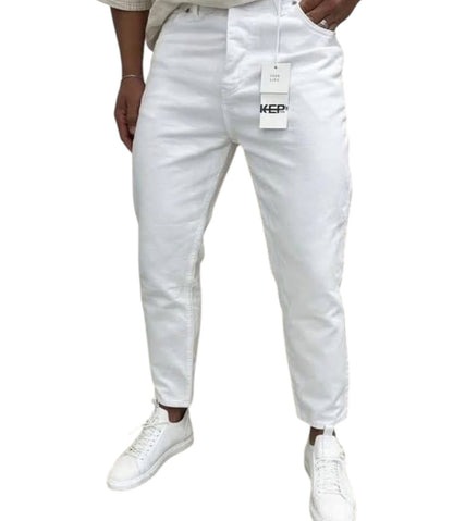 White slim-fit jeans with a visible hangtag and a white sneaker, shown on a model from the waist down against a plain white background.